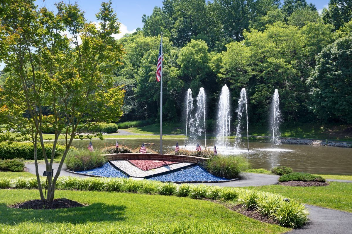 A serene park setting with a fountain and an American flag amidst lush greenery.
