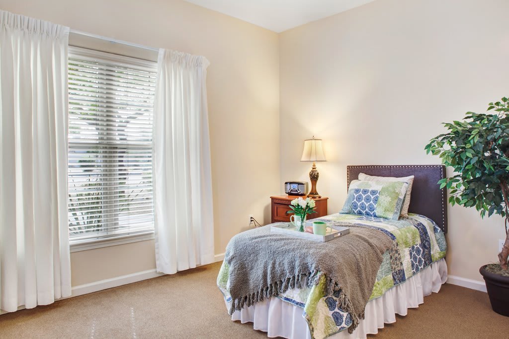 A cozy bedroom with a neatly made bed, a lamp on the nightstand, and a window with curtains.