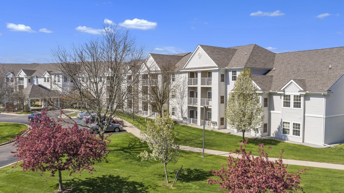 A scenic view of a residential apartment complex surrounded by greenery and trees under a clear blue sky.