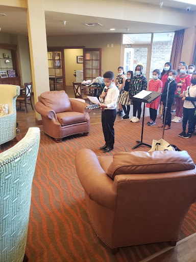 A group of children performing in a community space, with one boy reading from a sheet while others watch.