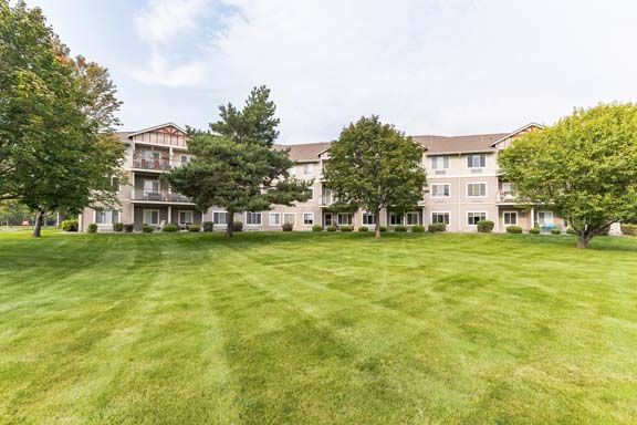 A residential apartment complex with a well-maintained lawn and surrounding trees.