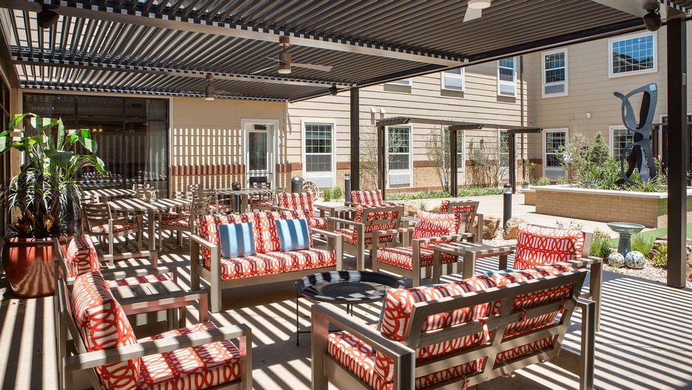 Outdoor patio area with colorful striped cushioned seating and a pergola providing shade.