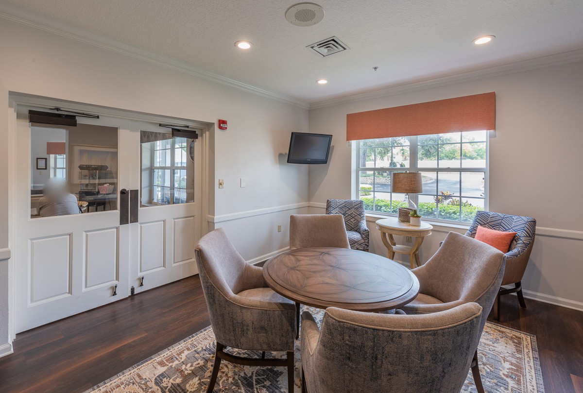 A cozy living room with a round table, four chairs, and a wall-mounted television.