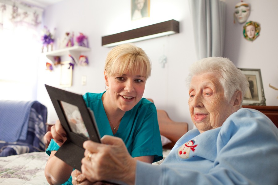 A caregiver assisting an elderly person while holding a framed picture.