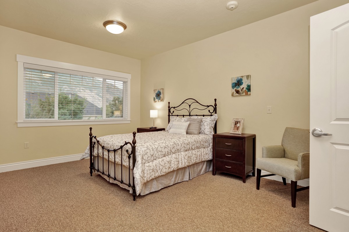 A cozy bedroom with a metal-framed bed, nightstand, and armchair.