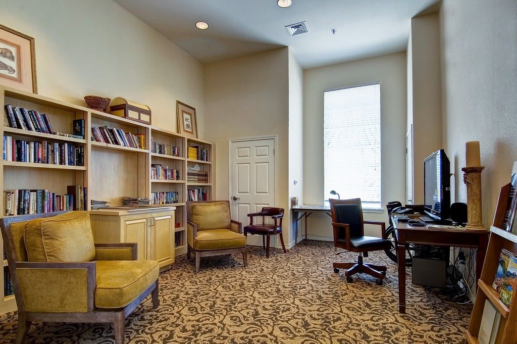 A cozy office space featuring bookshelves, comfortable chairs, and a desk by a large window.