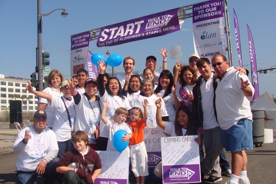 A group of people gathered at the start line of a charity walkathon, holding balloons and smiling.