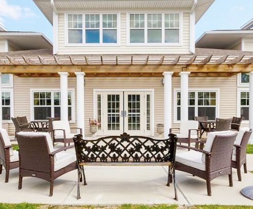 A beautifully designed patio area with outdoor furniture and a pergola, set in front of a stylish house.