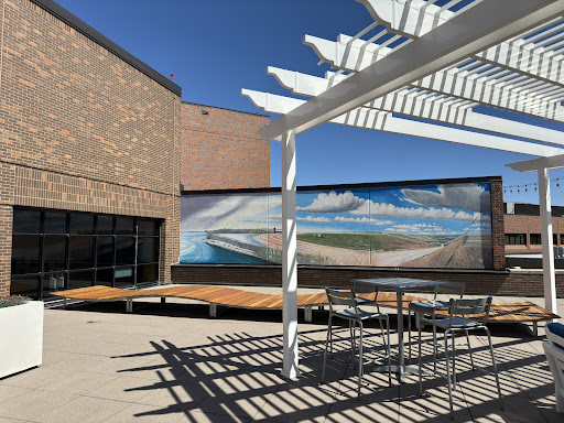 A sunny outdoor space featuring a wooden deck, modern architecture, and a vibrant mural in the background.