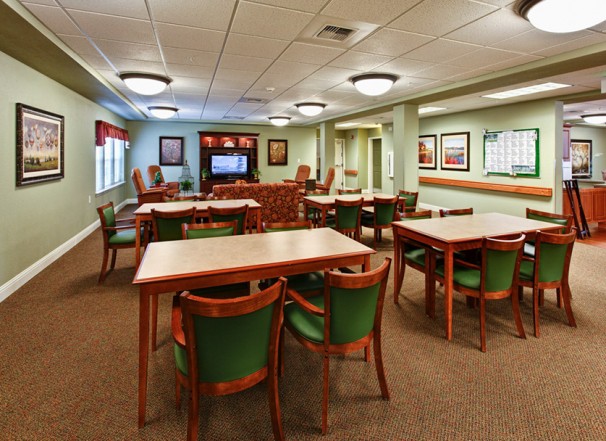 An empty dining area with wooden tables and chairs, carpeted flooring, and ceiling lights.