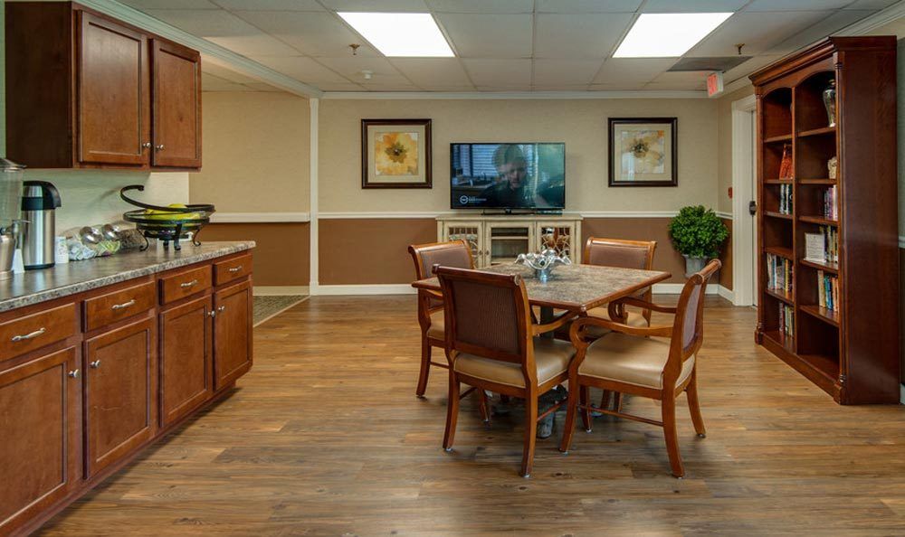 A cozy dining area with wooden flooring, featuring a table surrounded by chairs, a television on the wall, and decorative artwork.
