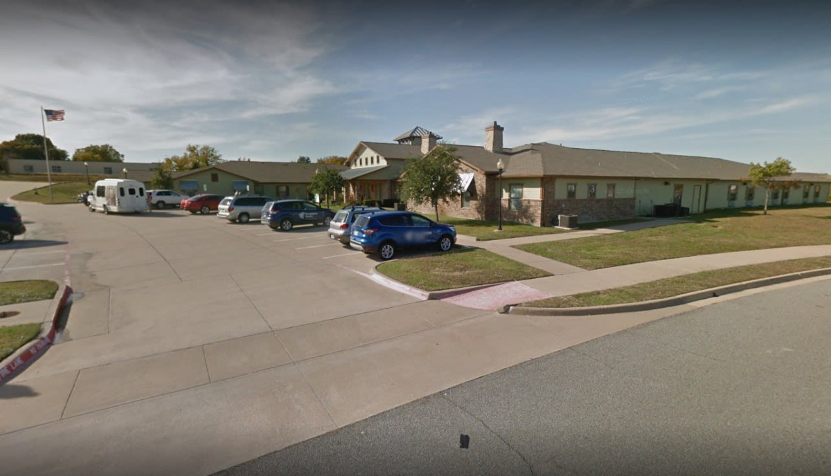 A suburban residential house with several cars parked in the driveway and a well-maintained lawn.