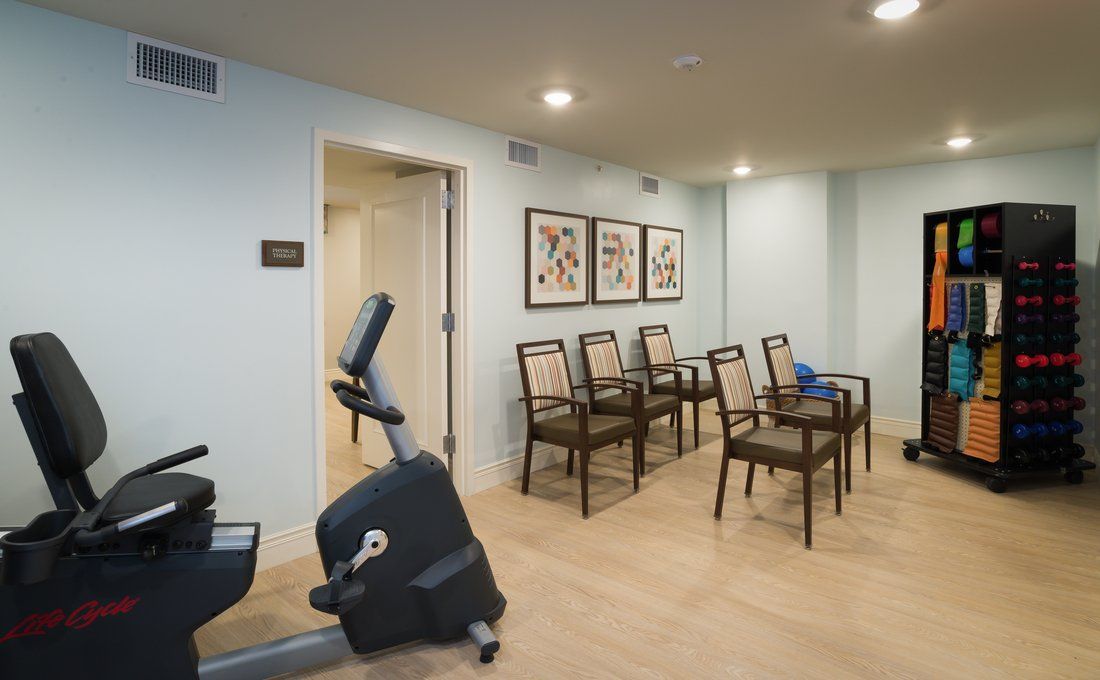 A small waiting area with an exercise bike and chairs against light blue walls, featuring framed wall art.