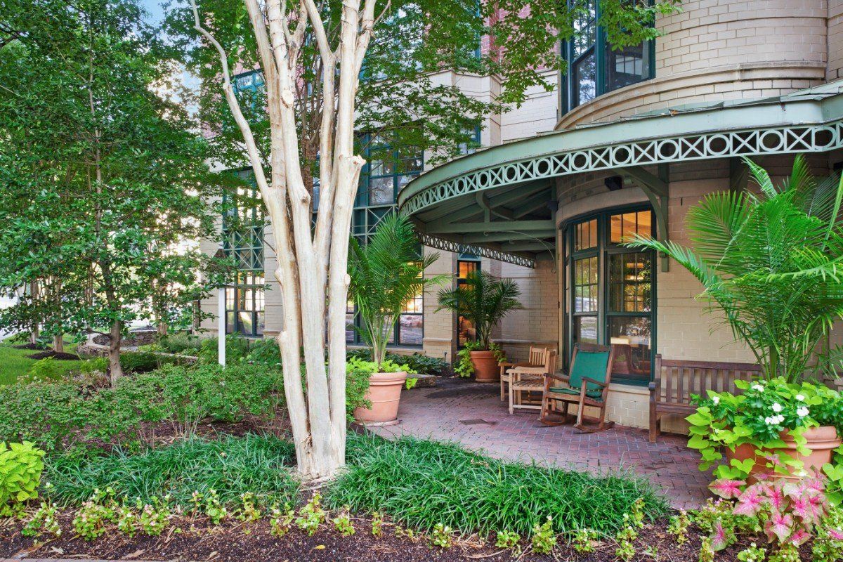 A charming porch surrounded by lush greenery and a garden, featuring outdoor seating.
