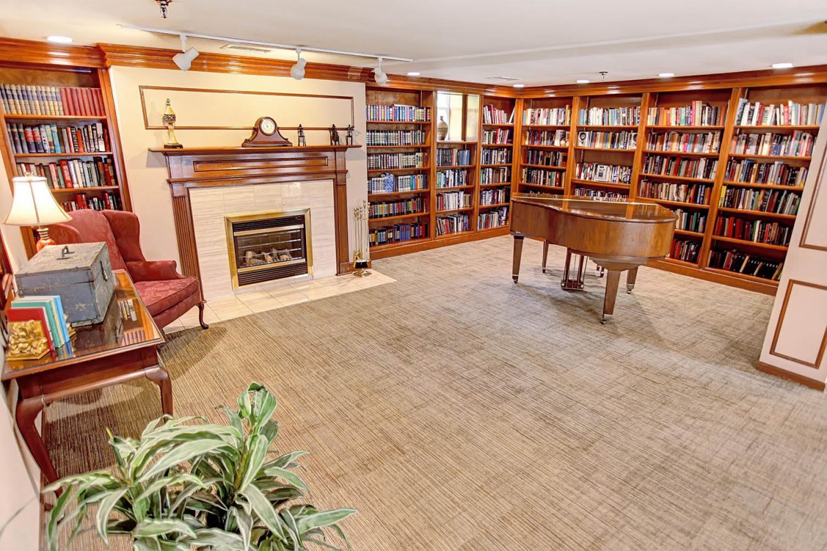 A cozy room with a grand piano, surrounded by bookshelves and a fireplace.