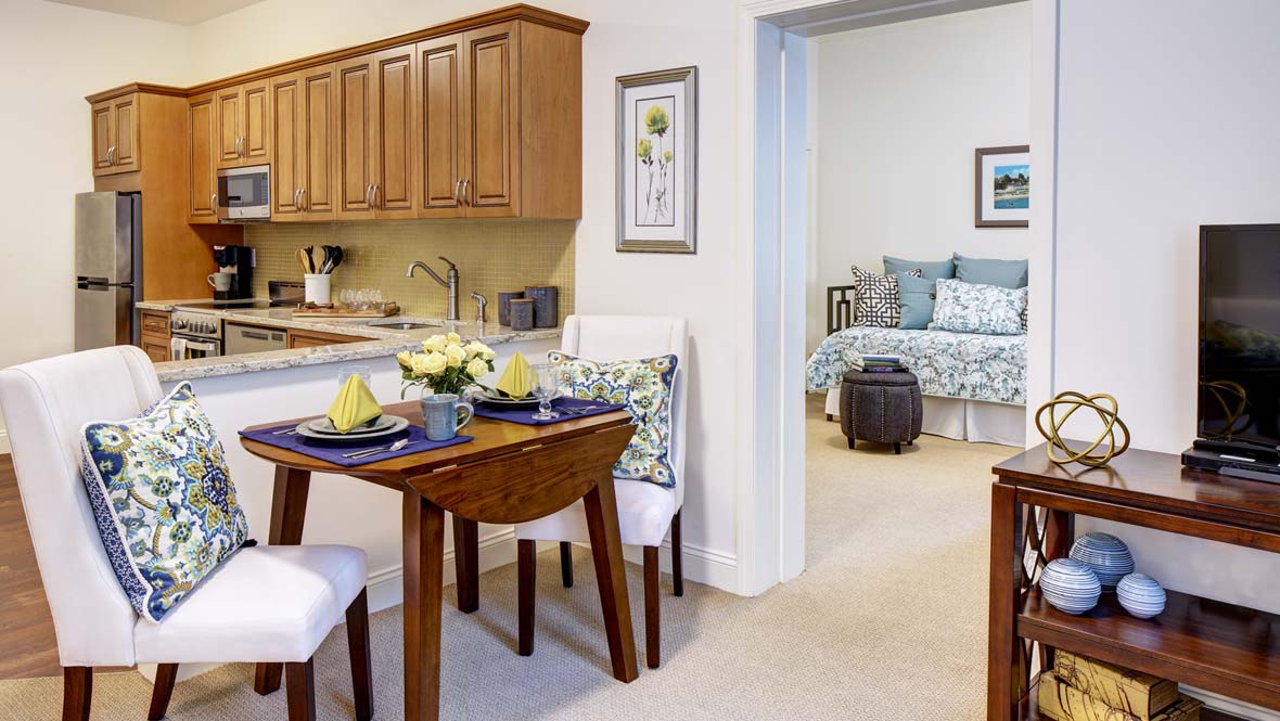 A cozy apartment with an open dining area leading to a bedroom, featuring wood cabinetry and stylish decor.