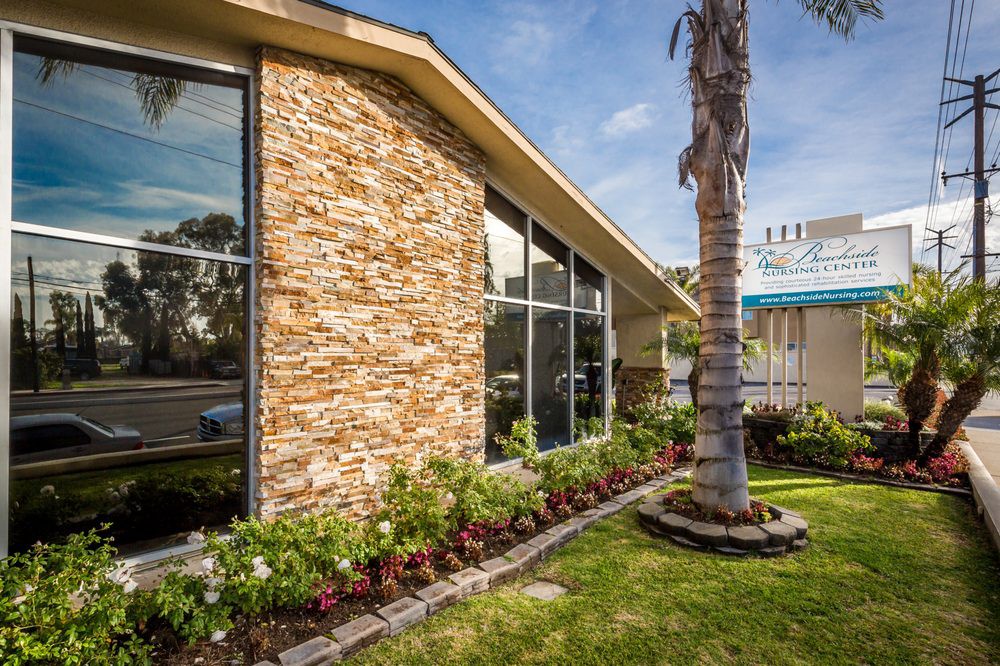 A modern building with a stone facade and large glass windows, surrounded by manicured landscaping featuring a palm tree.