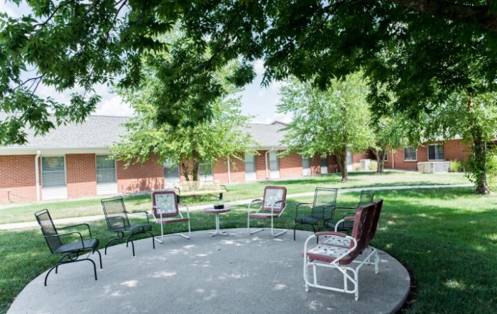 A peaceful outdoor patio area with chairs arranged under the shade of large trees.