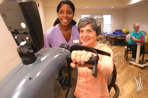A healthcare worker assists an elderly woman during her exercise session in a rehabilitation center.