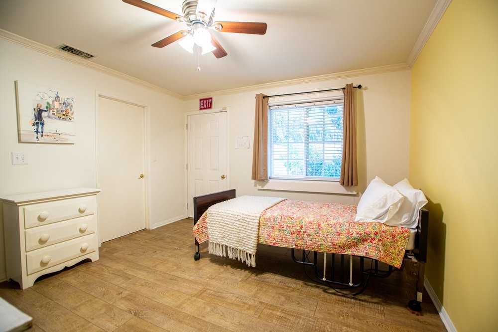 A minimalist bedroom with a single bed, wooden flooring, and a ceiling fan.