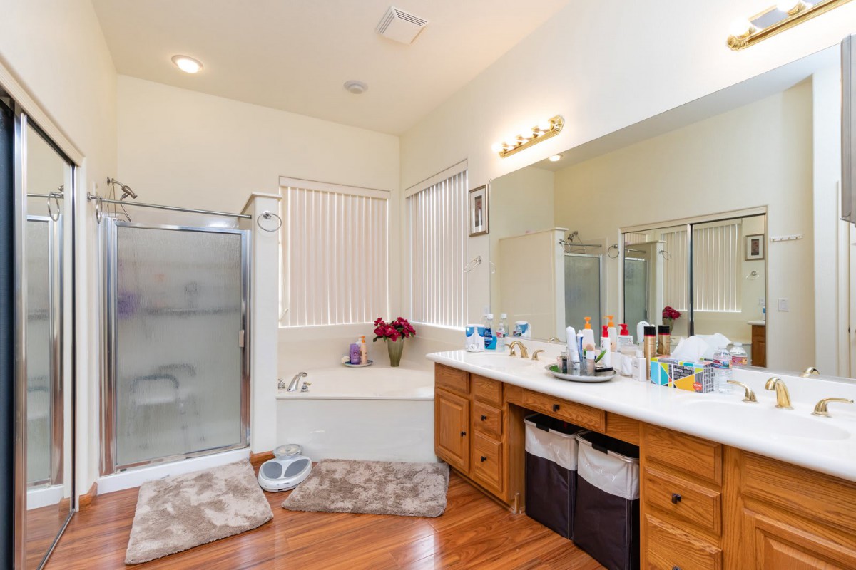 A spacious bathroom featuring a shower, bathtub, large mirror, and wooden vanity with multiple sinks.
