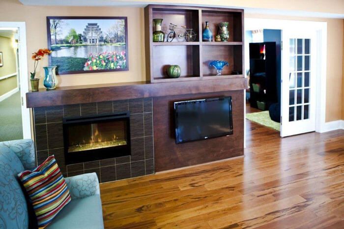 A cozy living room with a fireplace and mounted television, featuring decorative shelves and wood flooring.