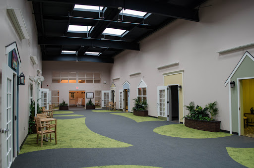 A spacious interior hallway featuring multiple doors, natural lighting from skylights, and a carpeted floor with green accents.