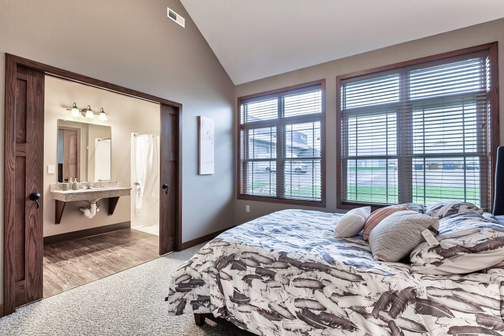 A modern bedroom featuring large windows that allow natural light to fill the space. The room is decorated with neutral colors and a comfortable bed, leading to an adjacent bathroom.