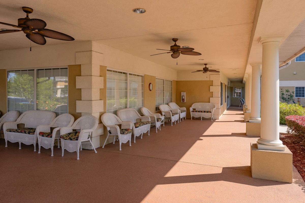A covered patio with white chairs and tables, featuring ceiling fans for cooling.