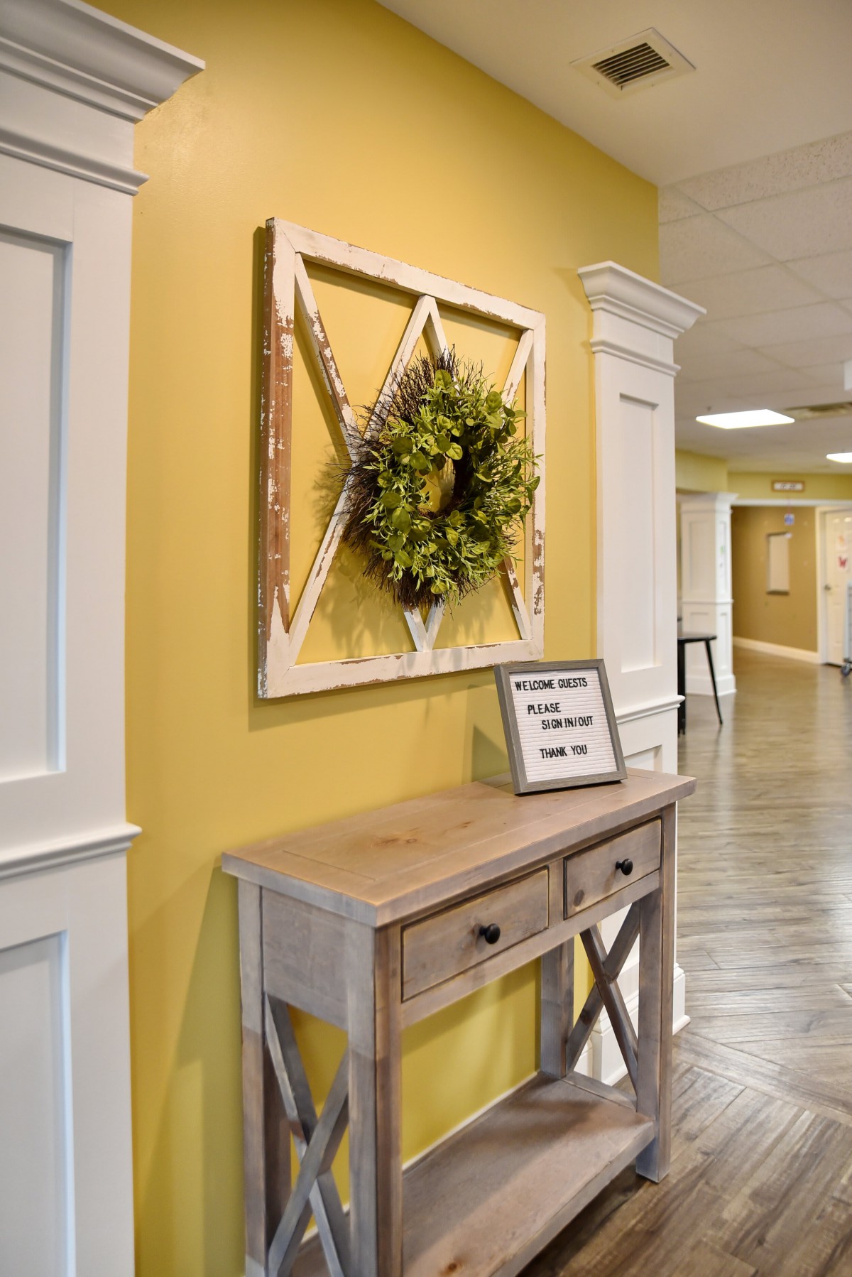 A hallway featuring a rustic table with decorative wall art and a wreath above.