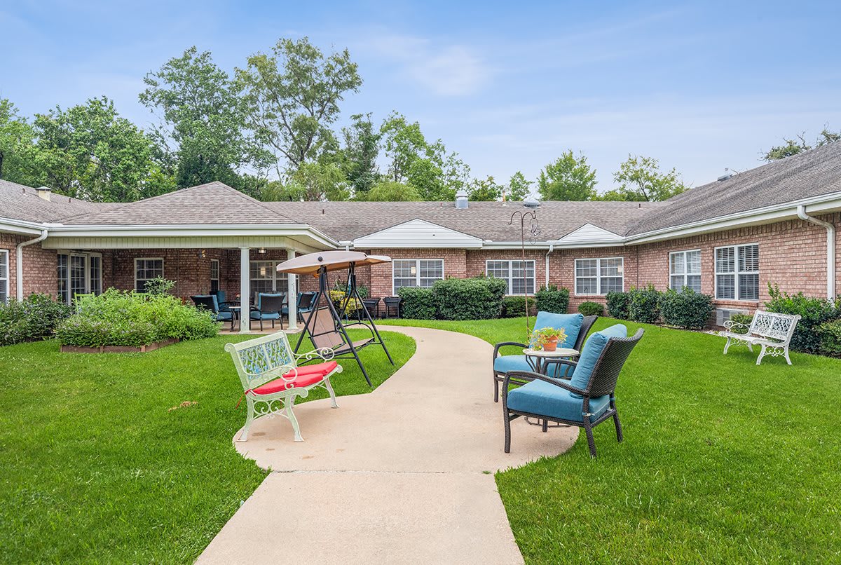 A well-maintained garden with a patio area, featuring comfortable chairs, a swing, and a paved pathway.