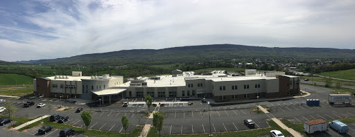 A panoramic view of a modern building surrounded by mountains and a spacious parking lot.