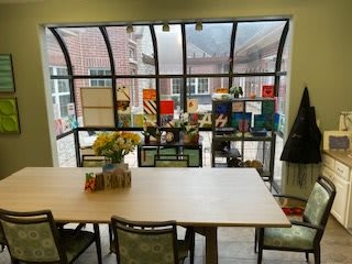 A dining area with a large table and chairs, set against expansive windows showcasing an outdoor view.