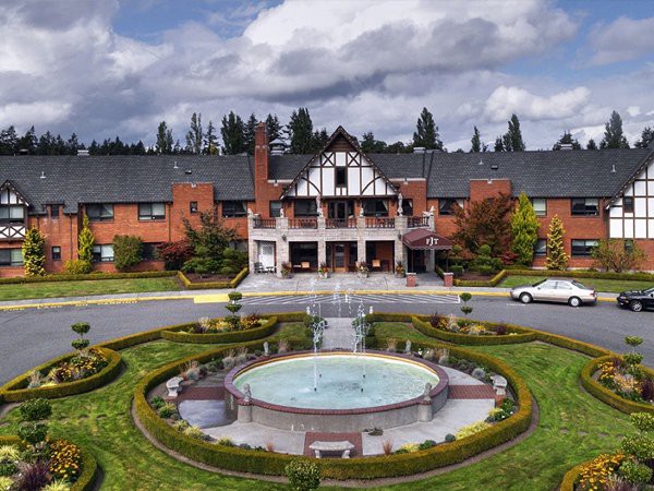 A grand hotel with Tudor-style architecture features a central circular fountain and well-maintained gardens.