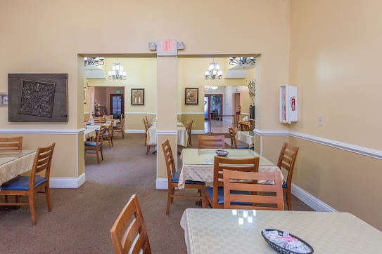 An indoor dining area with neatly arranged tables and chairs, illuminated by chandeliers.