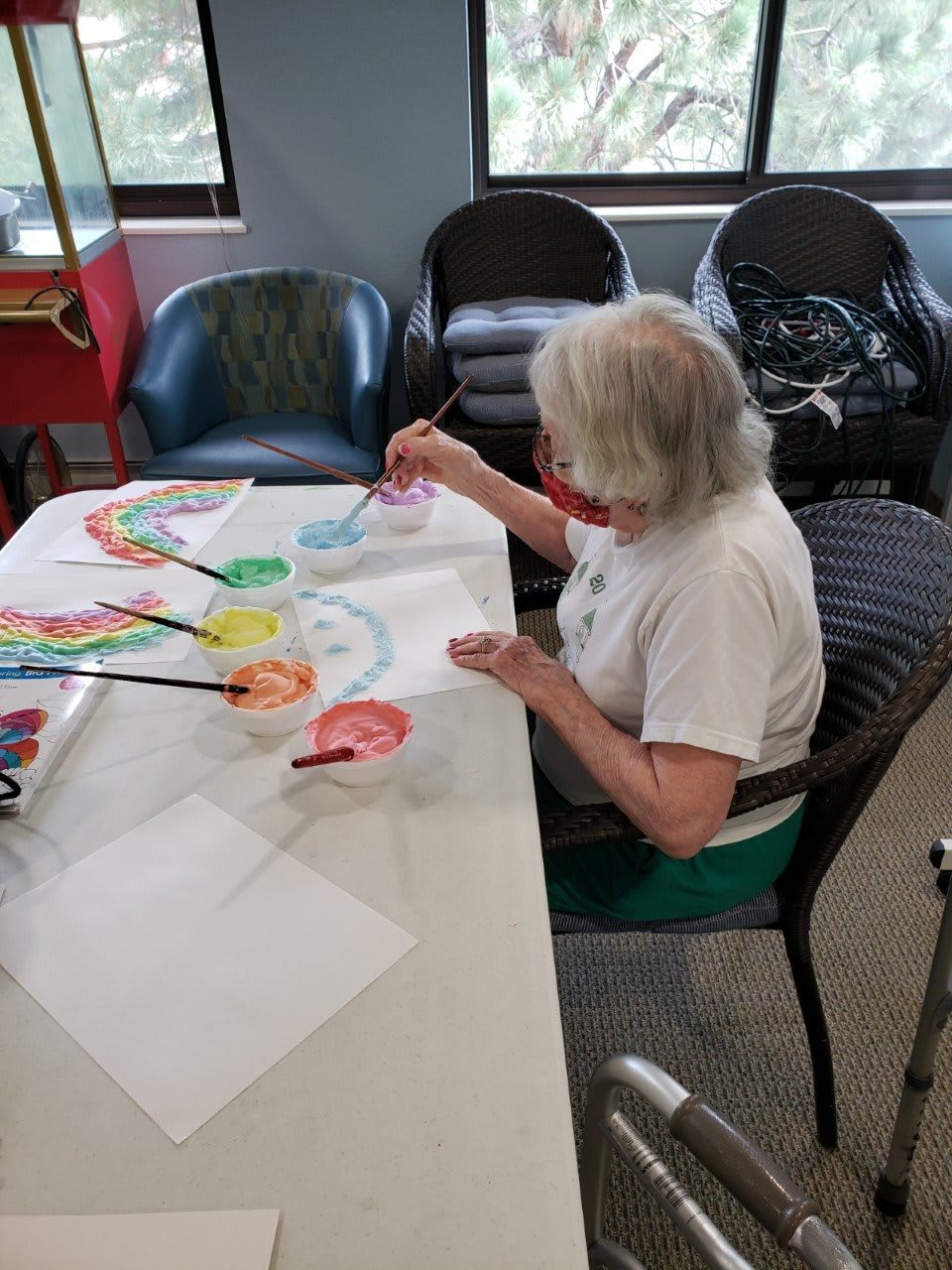 A senior woman engaged in painting a colorful artwork at a table indoors.