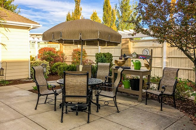 A cozy patio with a table, chairs, and an umbrella surrounded by plants.