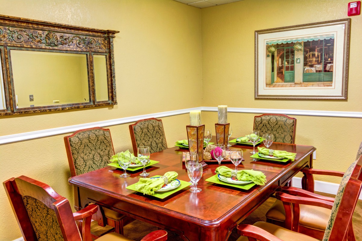 A warmly decorated dining room with a wooden table set for six, featuring green-themed place settings and decorative elements including a mirror and artwork on the walls.