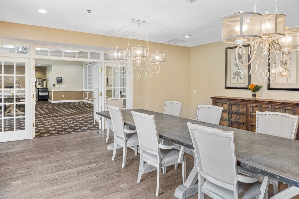 A well-lit dining room with a long table, white chairs, and a chandelier.