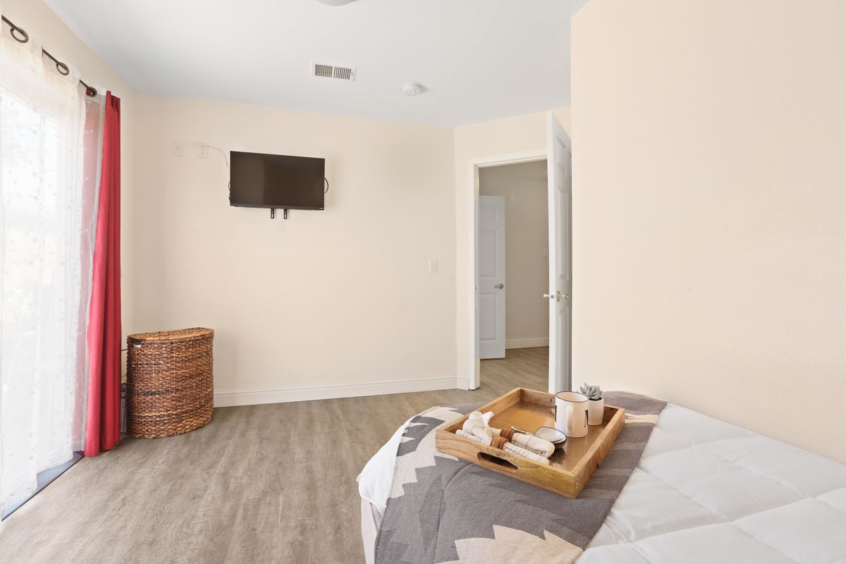 A minimalist bedroom featuring a mounted television, a wicker basket, and neatly arranged bedding with a wooden tray.