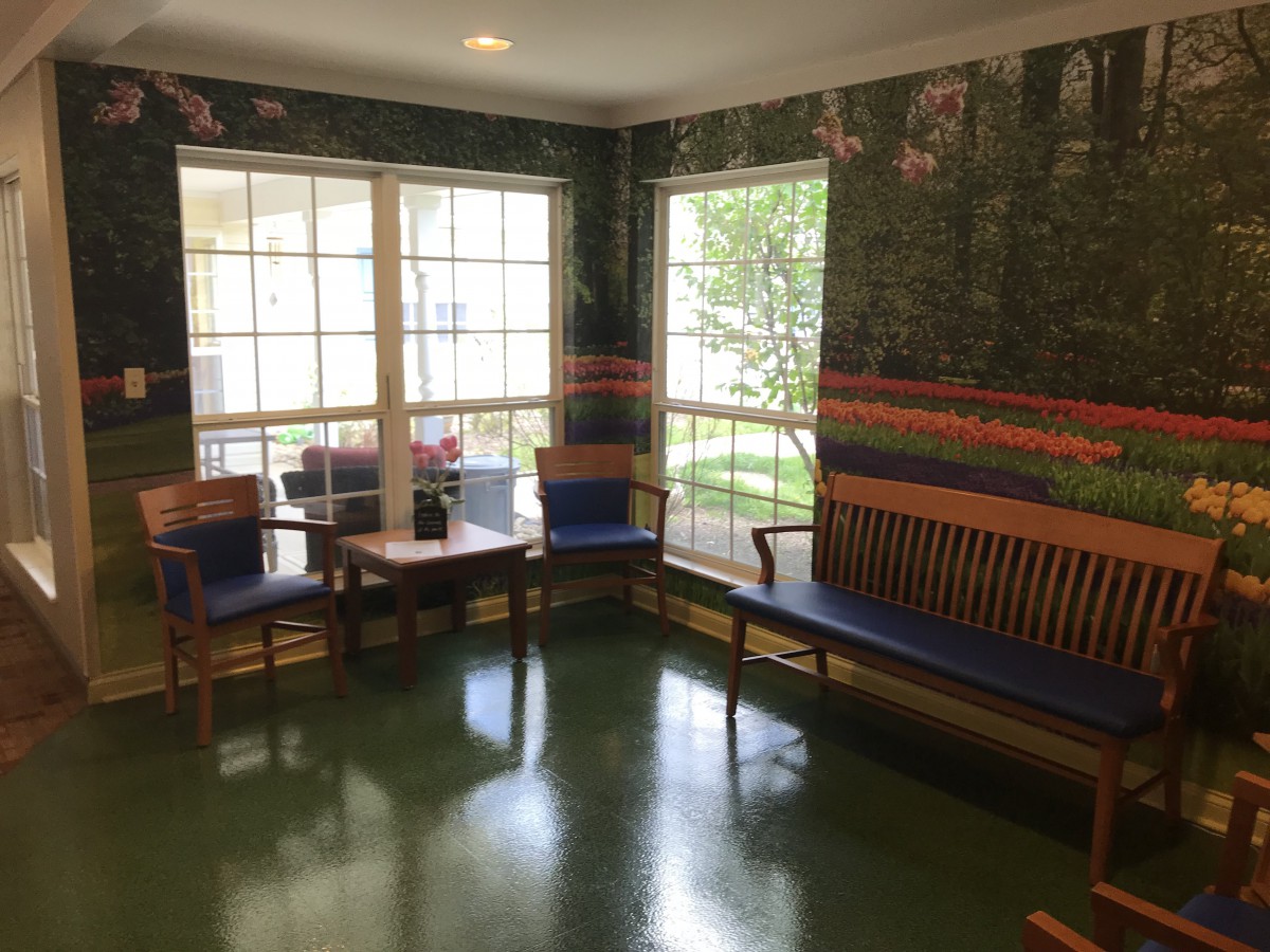 A cozy waiting room with chairs and a bench, illuminated by sunlight from large windows.