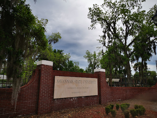 A view of a brick sign at the entrance surrounded by lush greenery under a cloudy sky.