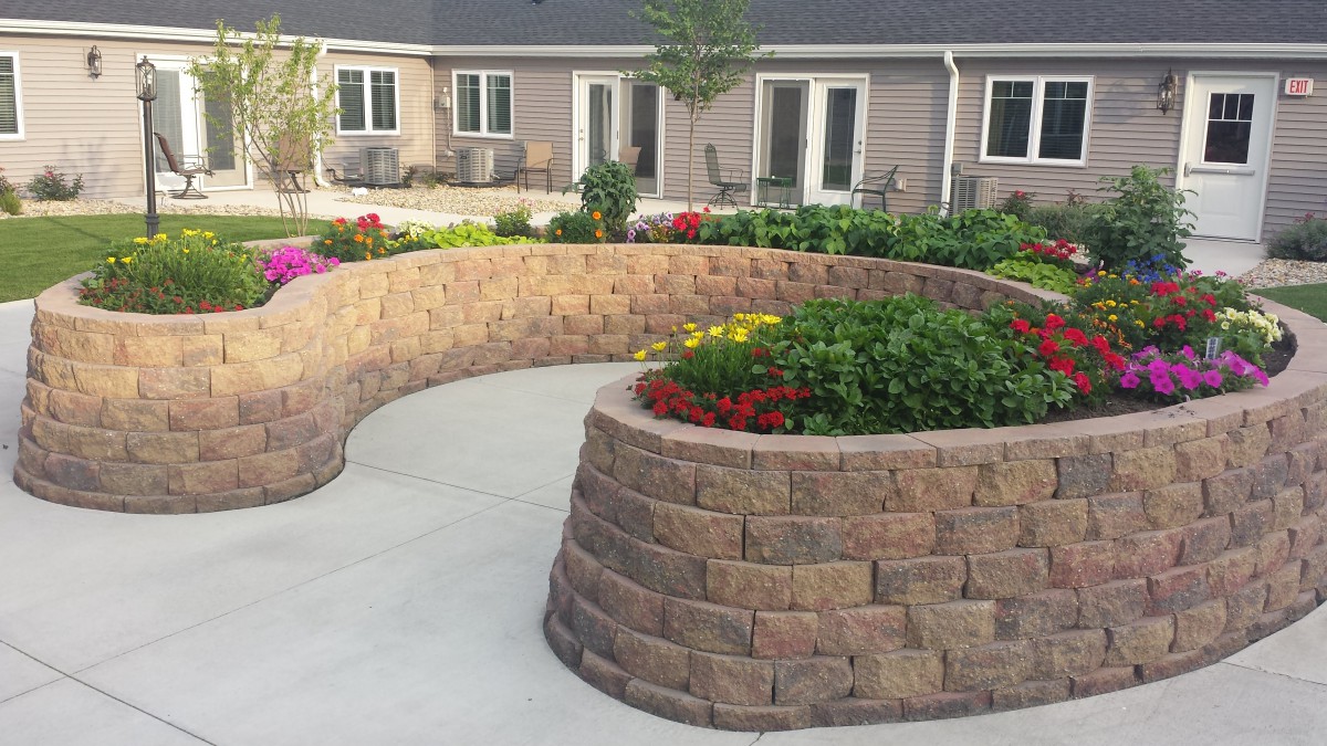 A beautifully landscaped garden featuring a curved retaining wall with vibrant flower beds.
