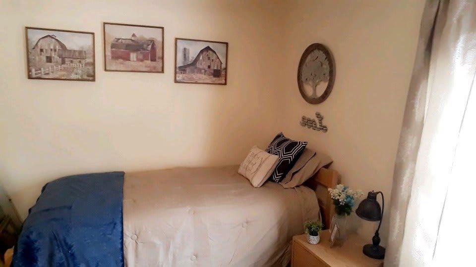 A cozy bedroom with wall art, a mirror, and a neatly arranged bed with pillows.