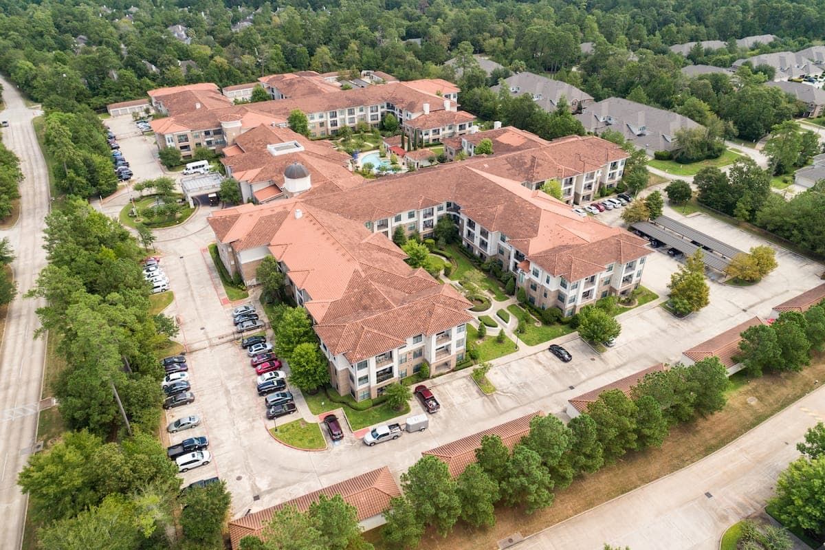 Aerial view of a residential complex surrounded by trees with parking areas.
