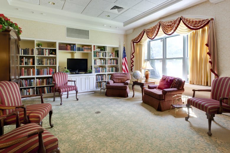 A cozy reading room with bookshelves, comfortable chairs, and large windows.