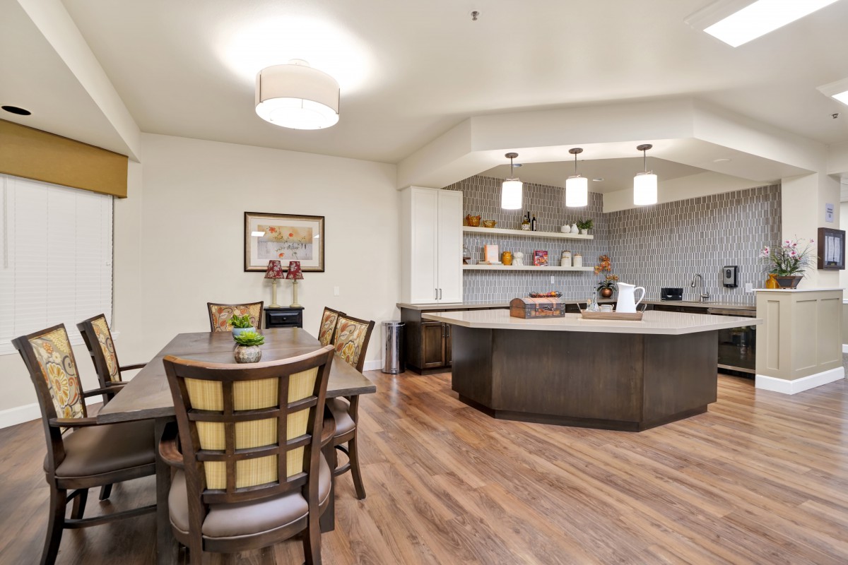 A modern open-concept dining and kitchen area with wooden flooring and pendant lighting.
