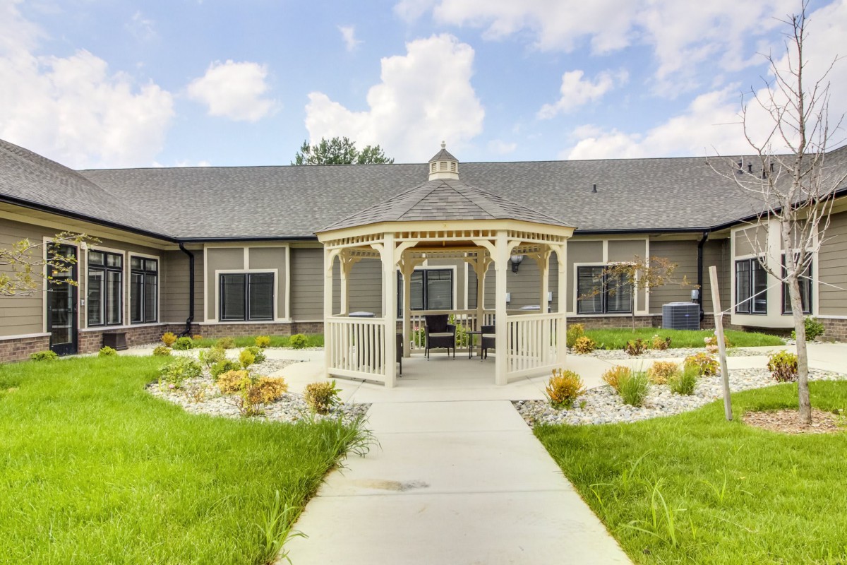 A beautiful gazebo surrounded by a landscaped garden and pathway leading to a building.