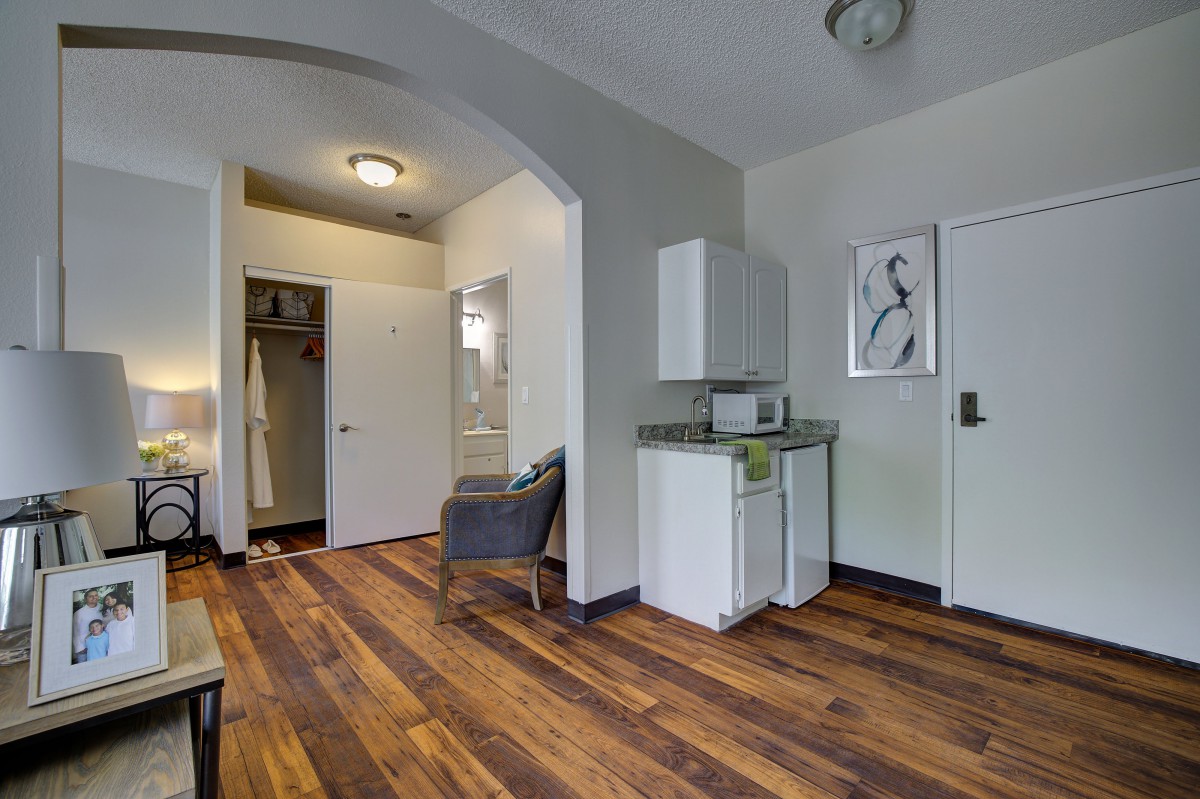 A modern apartment interior featuring a minimalist design with wooden flooring and a small kitchenette.