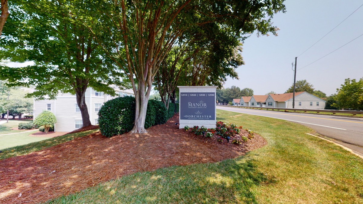 A sign for an apartment complex surrounded by trees and well-maintained landscaping.